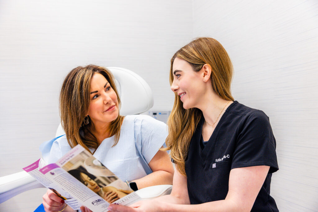Patient and provider reading an informational pamphlet during a consultation for plastic surgery near Flower Mound. The provider is explaining the risks of plastic surgery as well as pre- and post-care instructions and the expected recovery timeline.