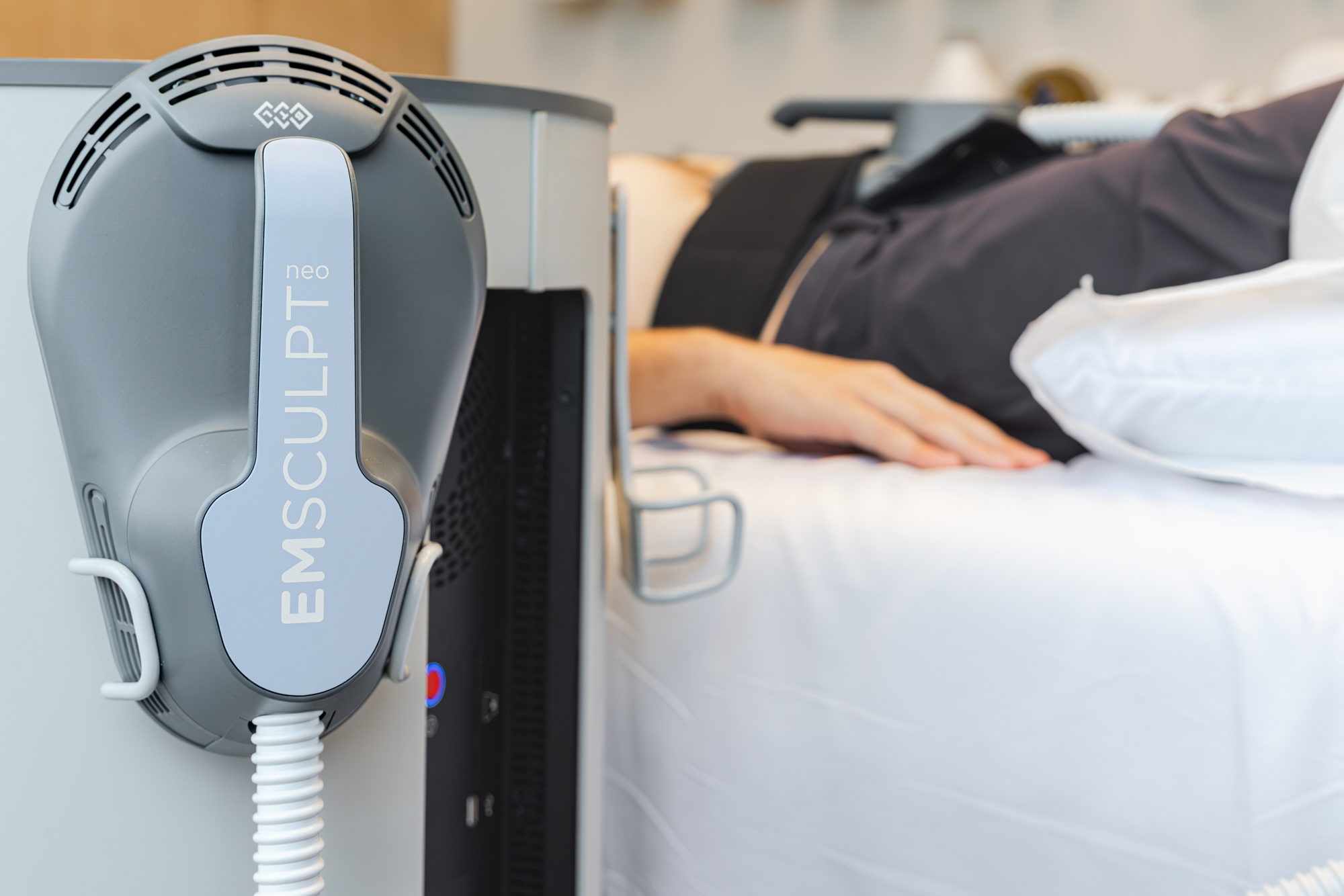 Emsculpt NEO handheld device placed in its holder as patient prepares lays in the background preparing for her appointment for a nonsurgical tummy tuck in Plano.