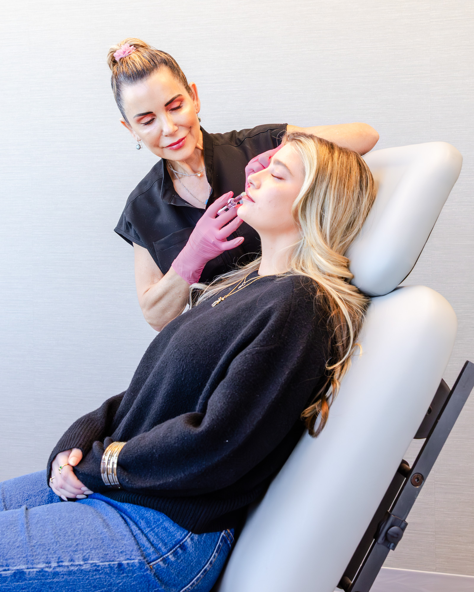 Patient leans back against treatment chair as her provider assesses her skin.