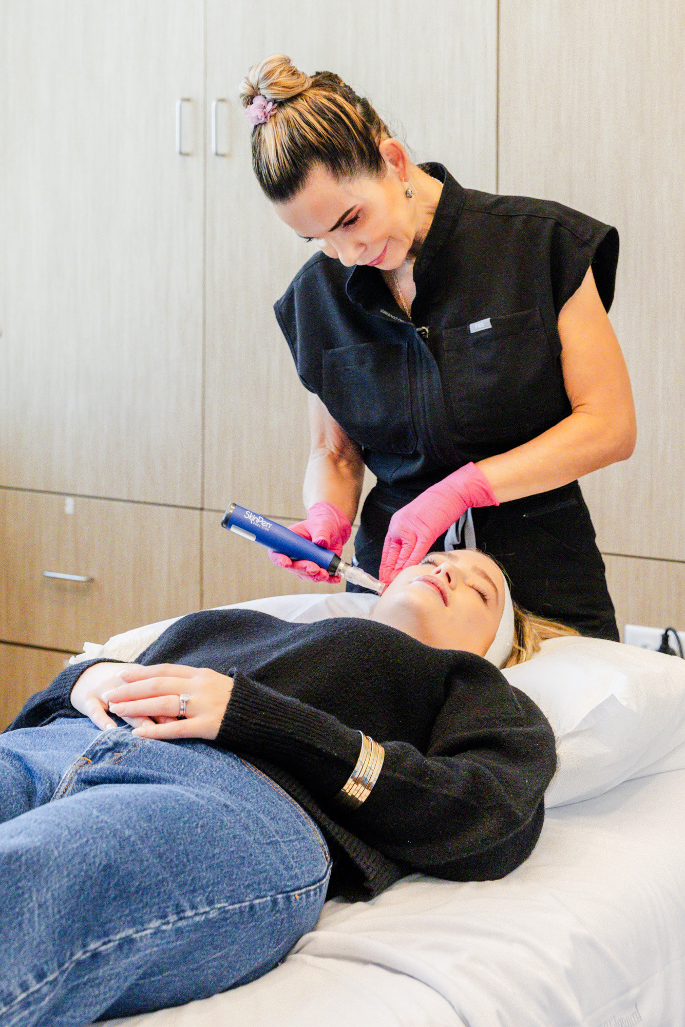 Patient lays back on treatment table as her provider performs a treatment for microneedling to improve the tone and texture of her skin.