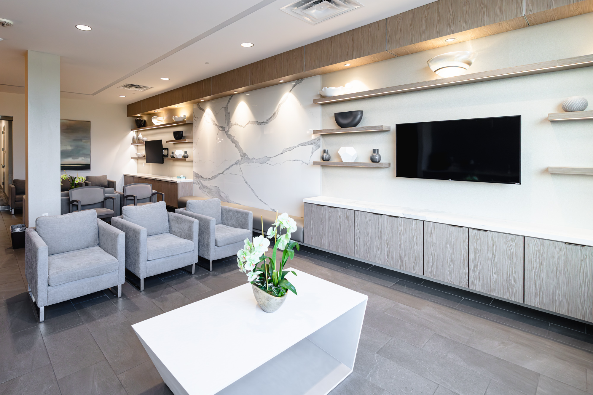 Lobby of office for a rosacea dermatologist in Frisco with 3 comfortable and inviting chairs, a table with flowers, and a television on the wall