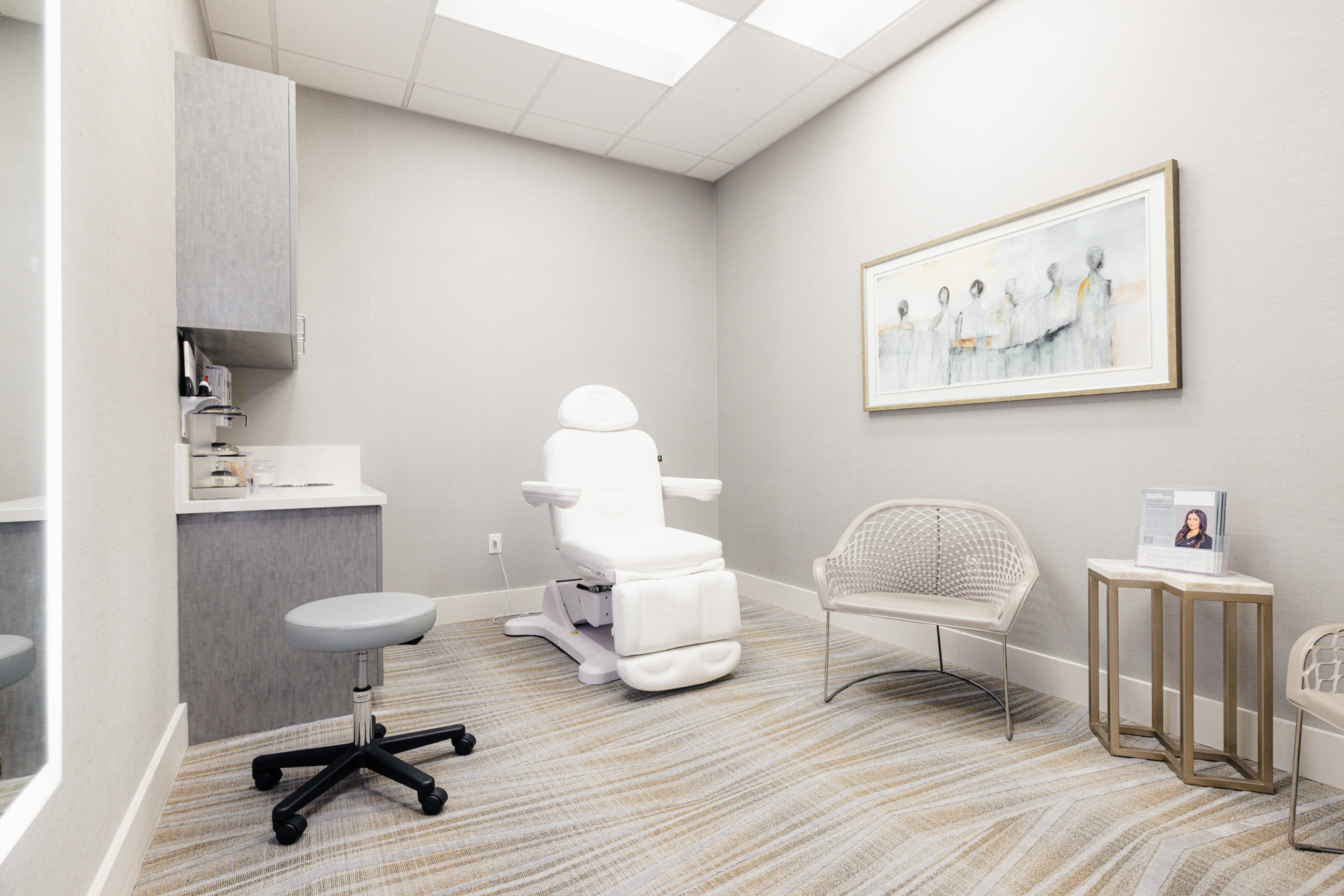 Treatment room at McGuiness Dermatology and Plastic Surgery where patients can get chin filler near Frisco. There is a photo on the wall, a treatment chair, and a rolling chair for the doctor to sit.