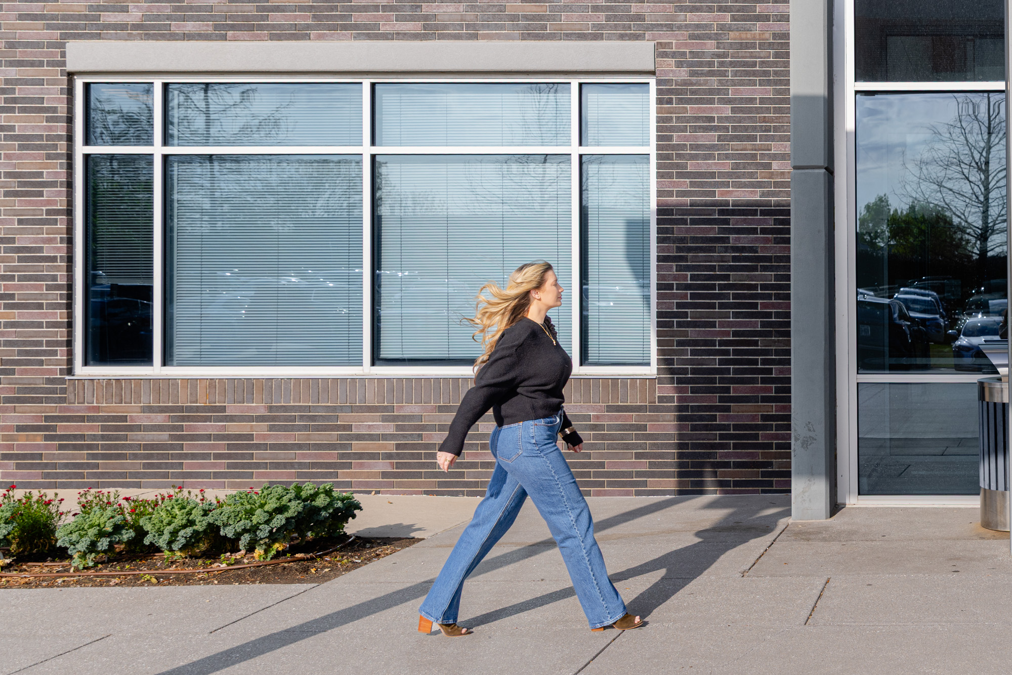 Woman walking confidently past a brick building after finishing her treatment for a nonsurgical tummy tuck in Plano.