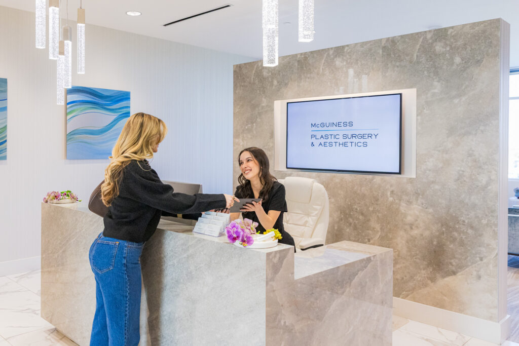 Patient and receptionist at the check-in desk at McGuiness Plastic Surgery & Aesthetics. The patient is returning a tablet where she filled out a questionnaire explaining why she's interested in plastic surgery near Frisco.