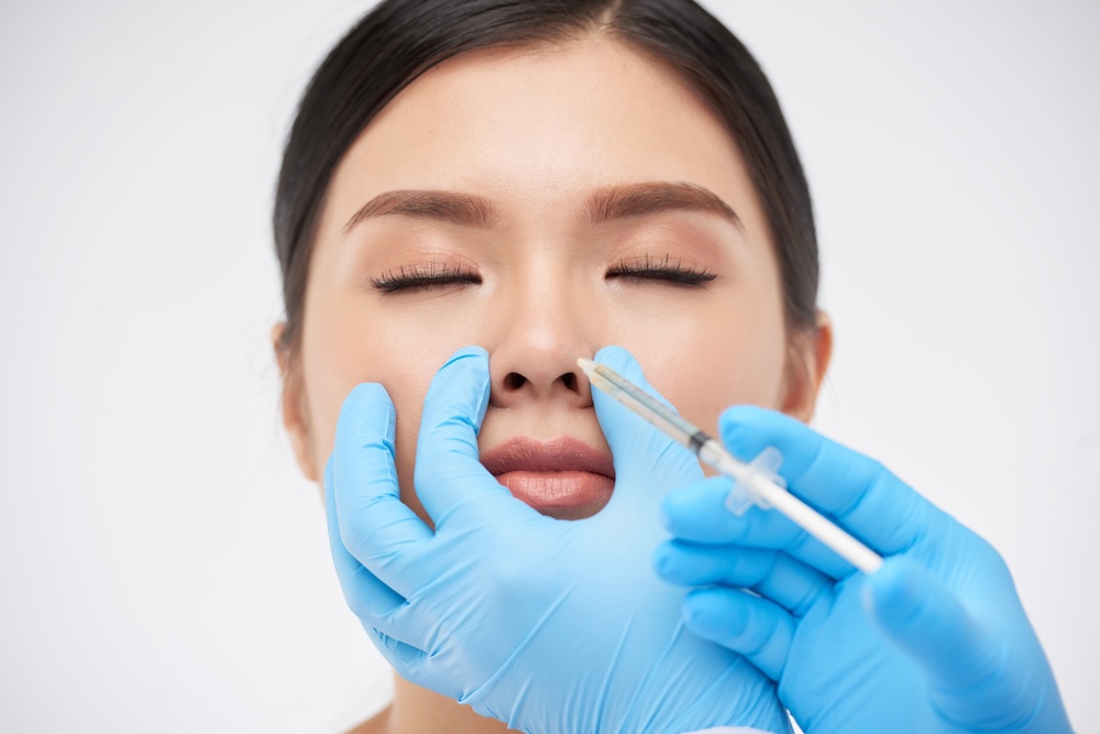 Young woman has eyes closed as an injector places dermal filler in her nose for a nonsurgical rhinoplasty in Plano