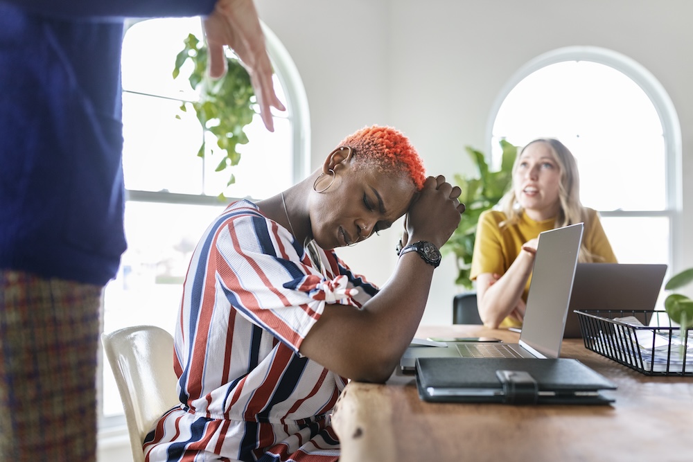 Woman has head on hands and looks stressed out while at a work meeting. This stress can contribute to clogged pores and cause her to seek hormonal pimple treatment in Plano.