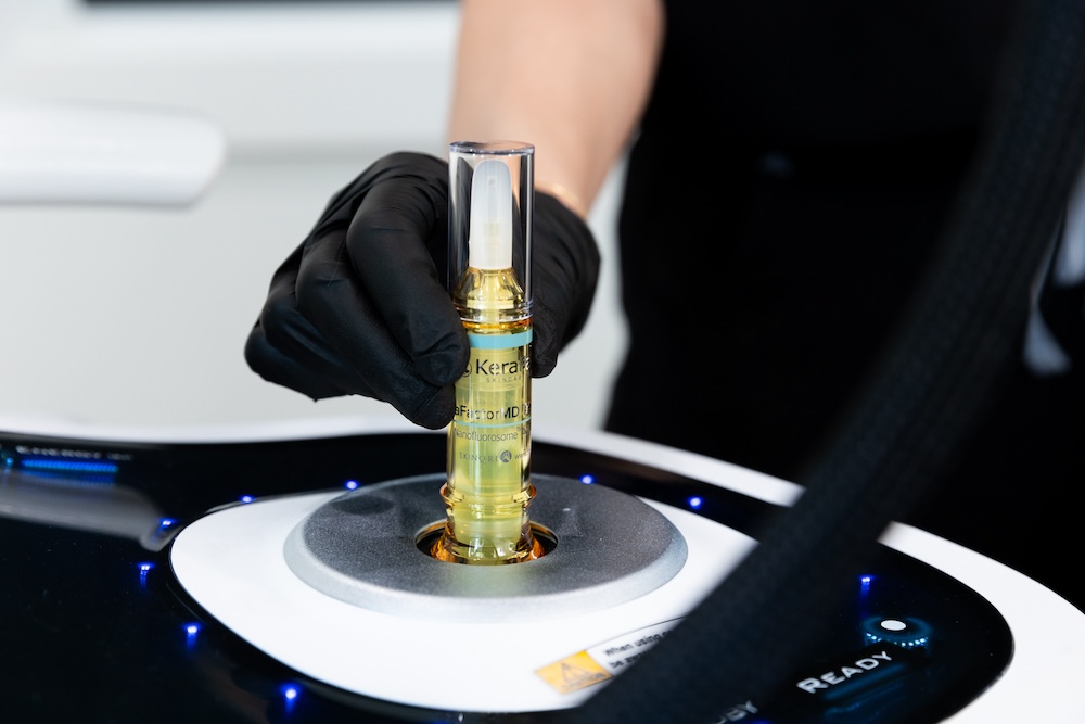 Professional wearing gloves holds a bottle of serum for nonsurgical hair restoration in Plano.