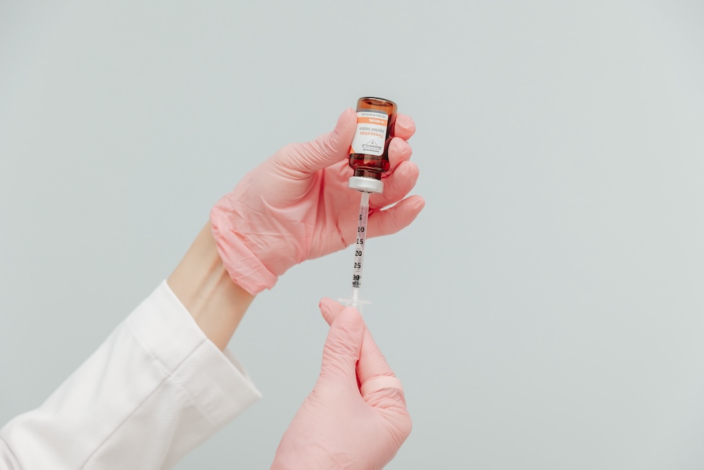 Provider wearing gloves holds a bottle containing GLP-1 in Plano in one hand, and a needle and syringe in the other.